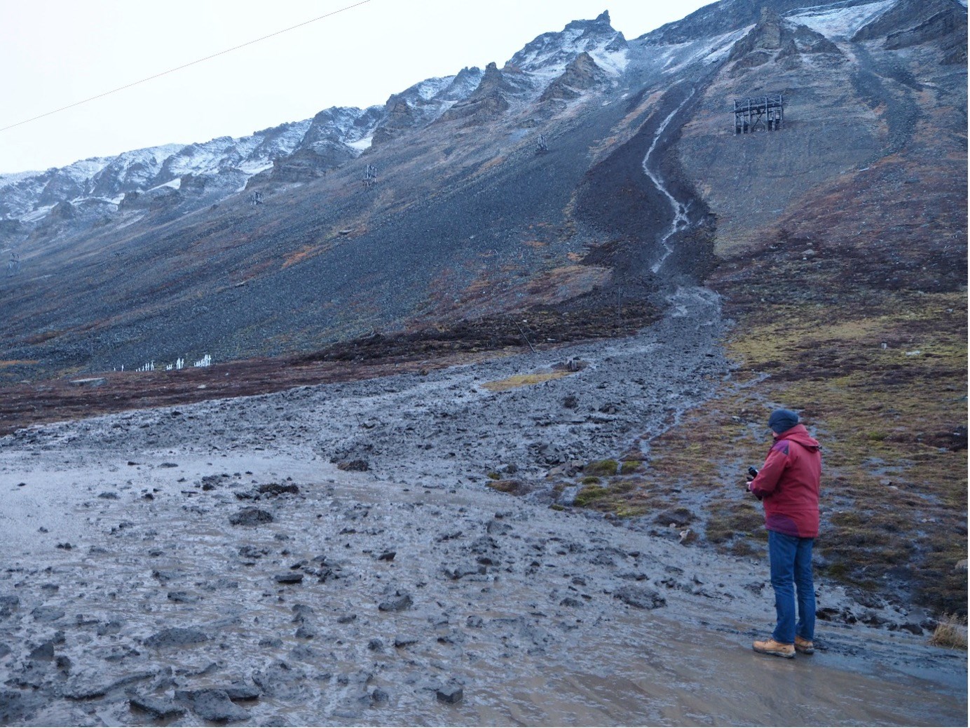 Aktivlagsskred i fjeldsiden i Longyeardalen i oktober 2016. Skredet kom ned blot 20 meter fra kirkegården, som også ses på fotoet. Personen står på vejbanen, som blev helt blokeret af skredmasserne.